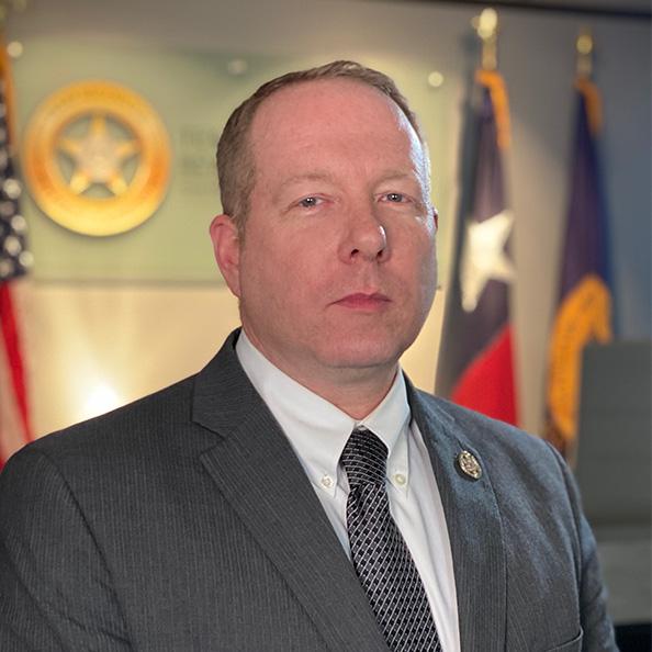 Ron Swenson in front of TABC logo, Texas flag, US flag.