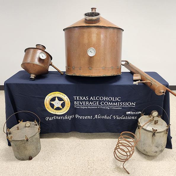 Different sections of a copper and grey still are splayed out on a table covered with a TABC-branded navy blue tablecloth.