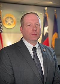 Ron Swenson in front of TABC logo, Texas flag, US flag.